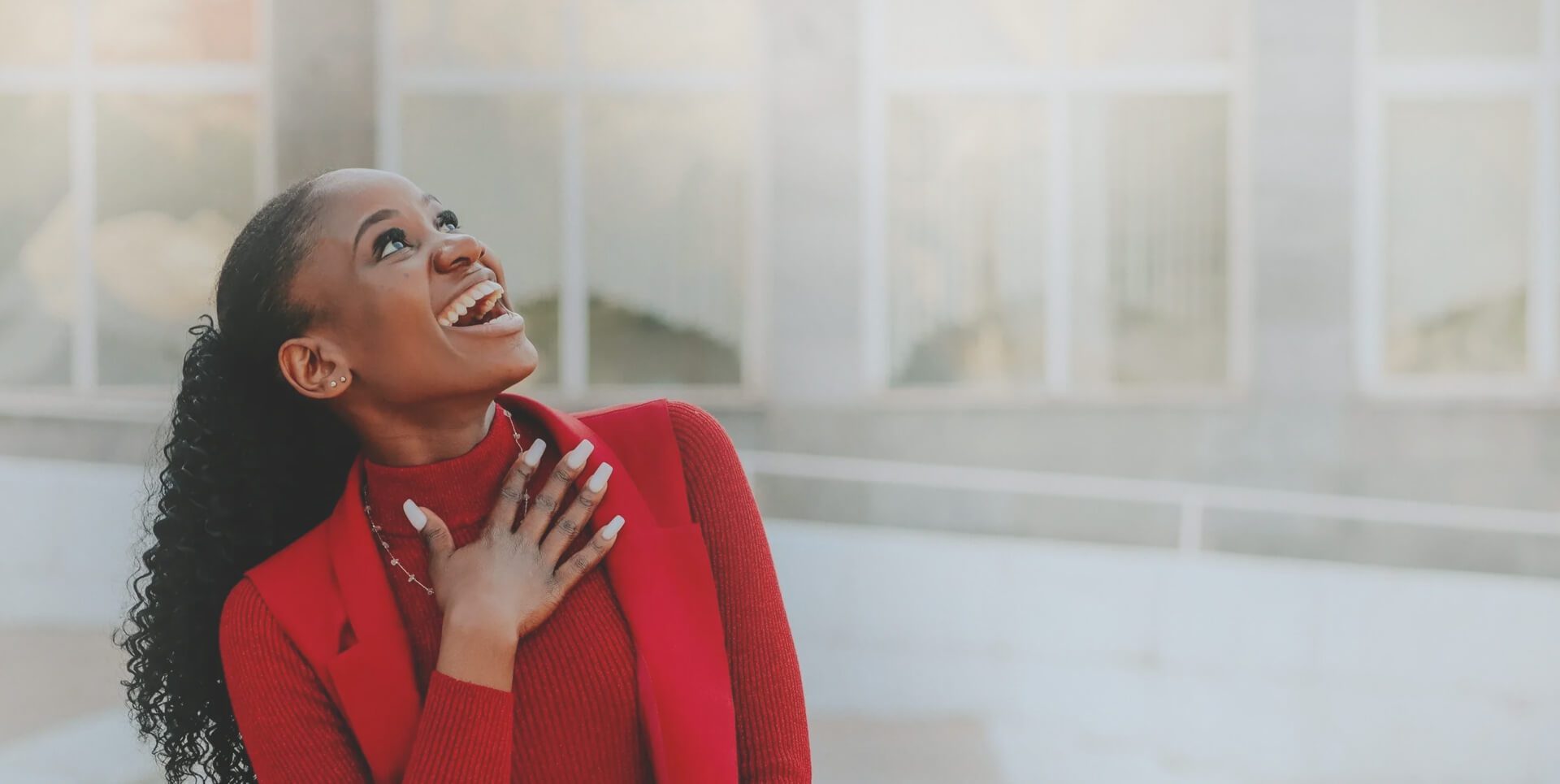 A woman in red jacket smiling and holding her hand to the side.