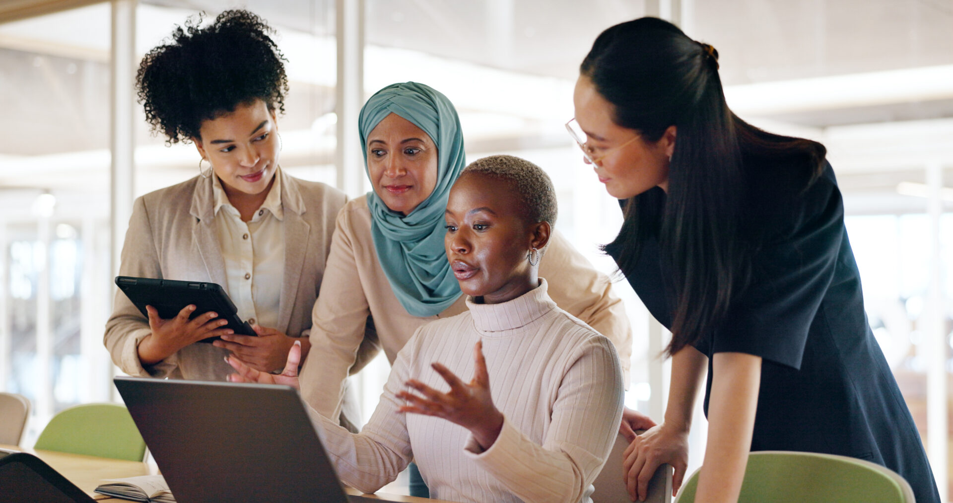 A group of women are gathered around a laptop.